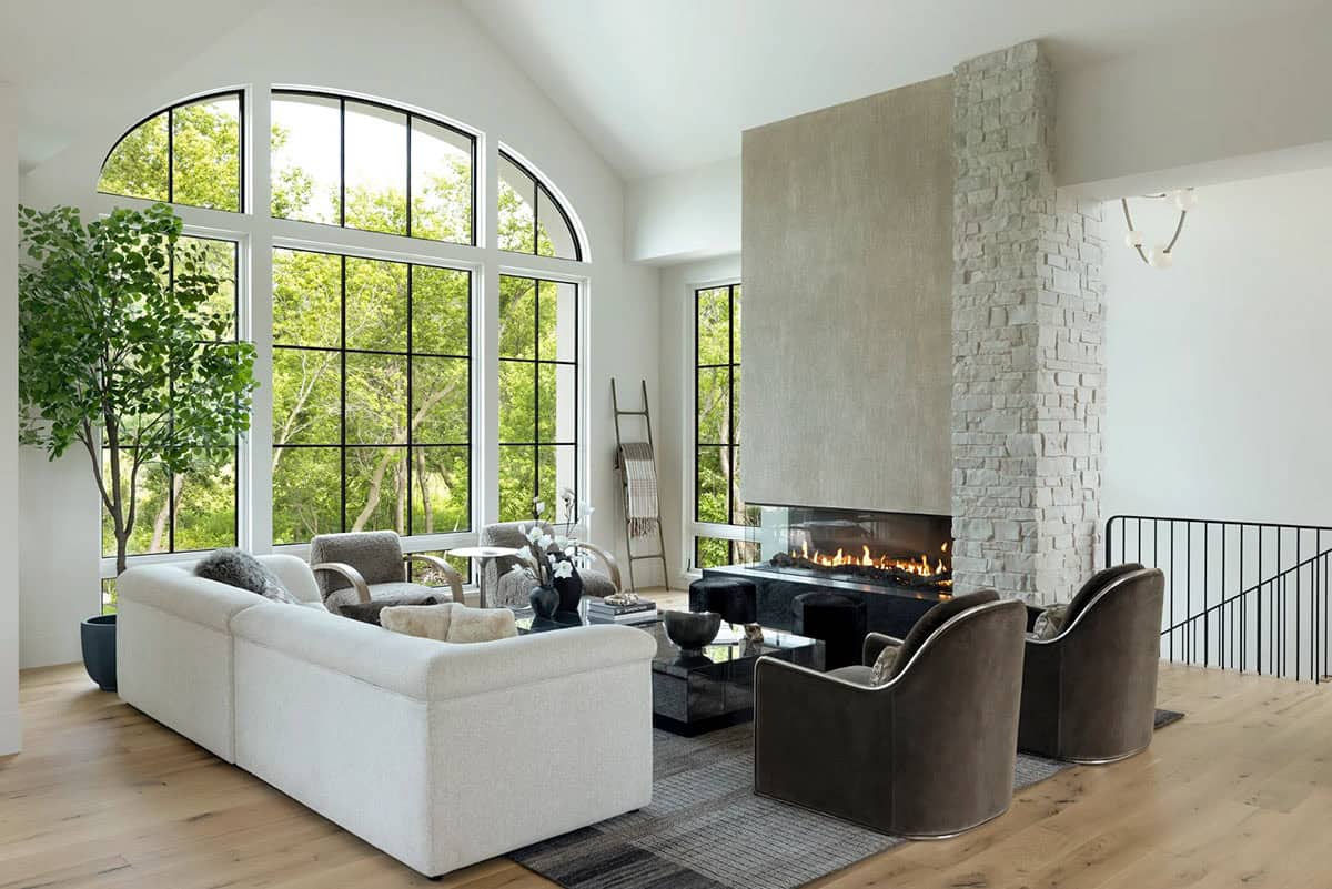 Living room with cream sectional, arched windows, and fireplace with stone column
