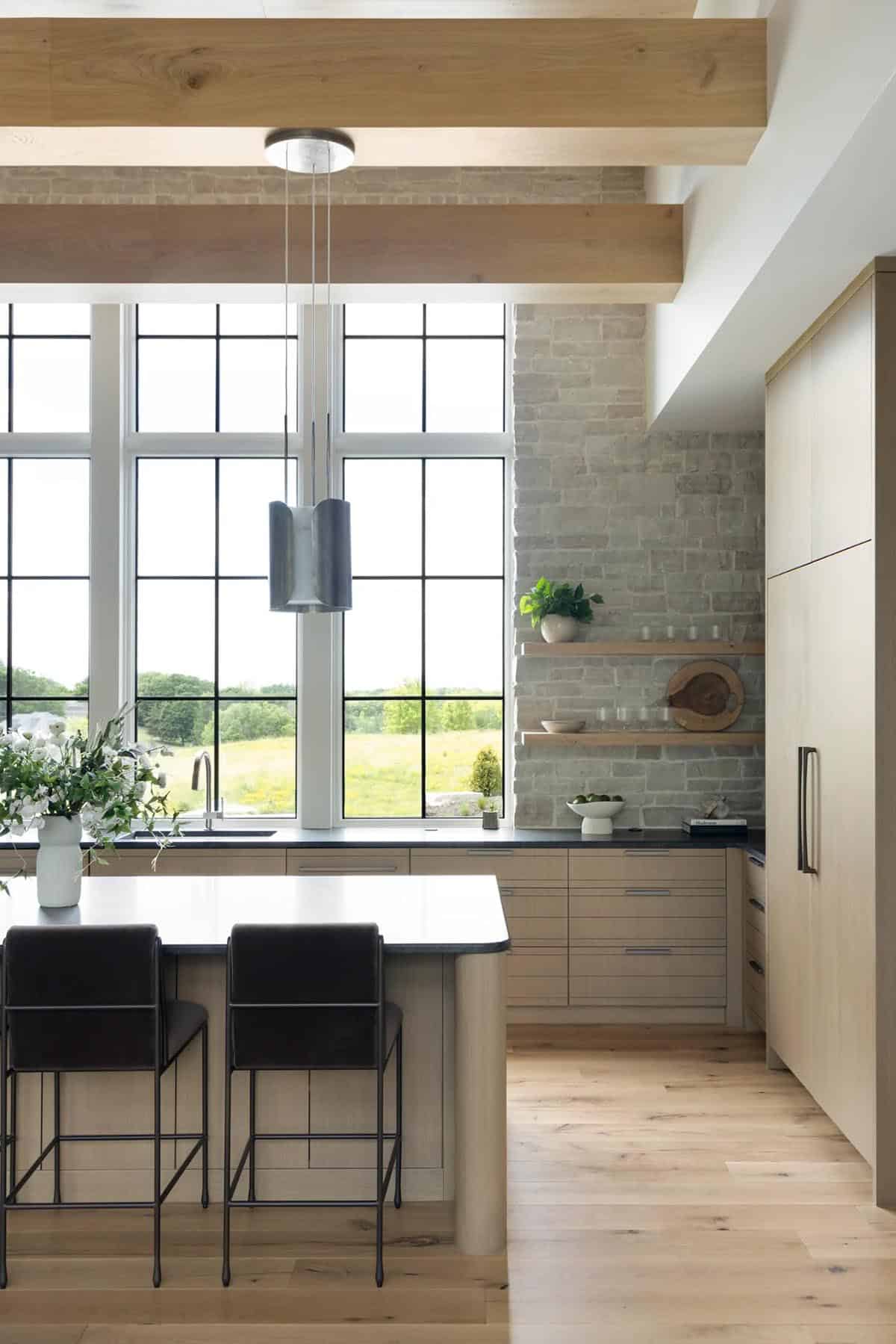 Kitchen island with leather stools beneath tall windows and stone wall