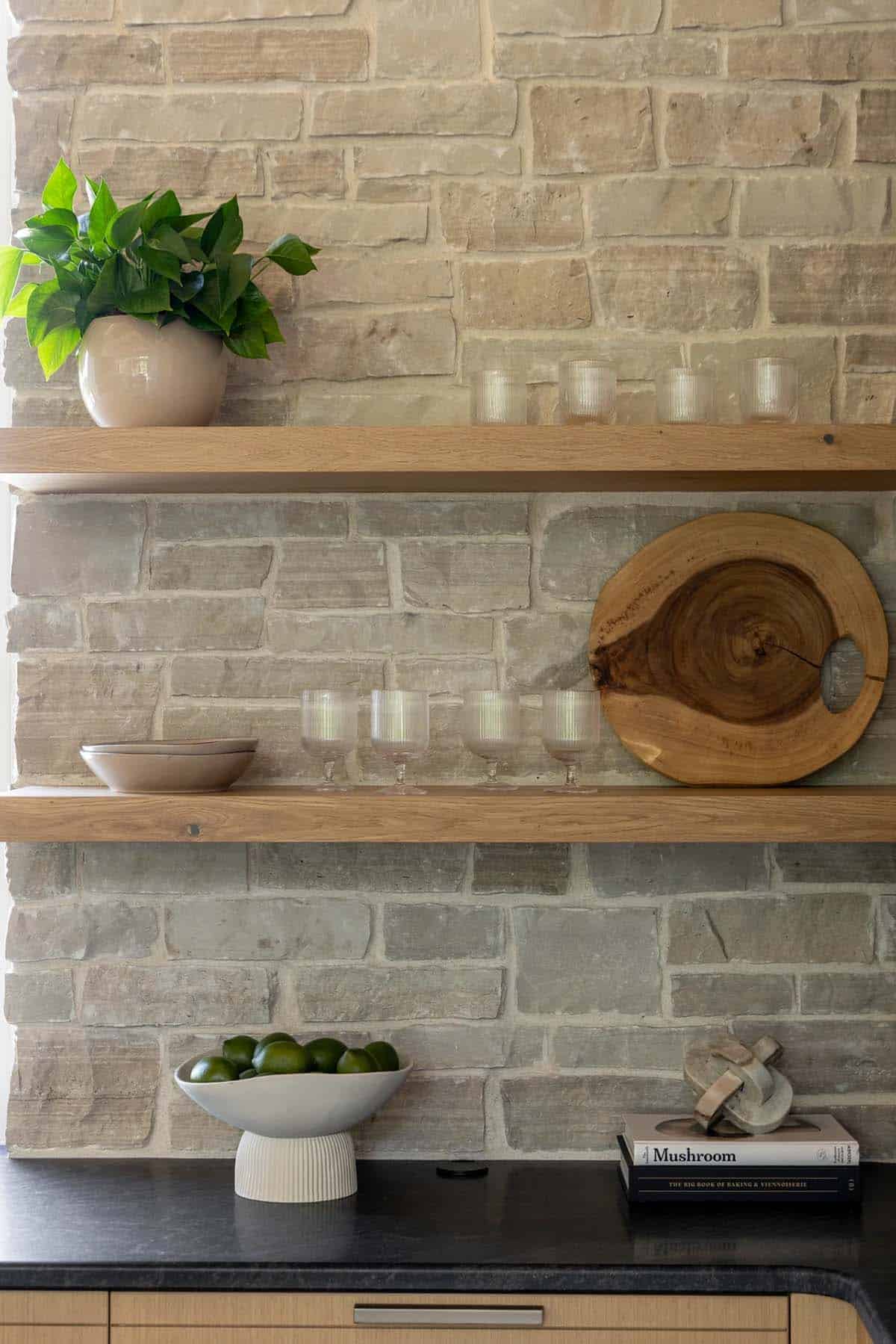 Floating oak shelves on stone wall with glassware and live edge board