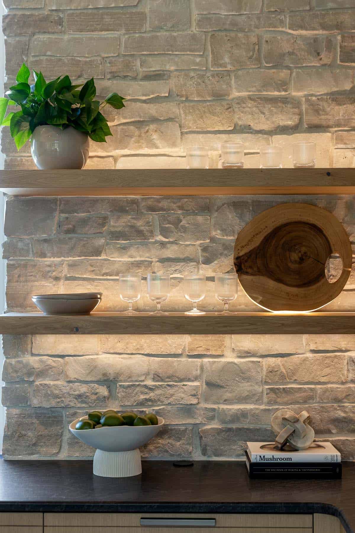 Under-shelf lighting highlighting stone wall, glassware, and wood serving board