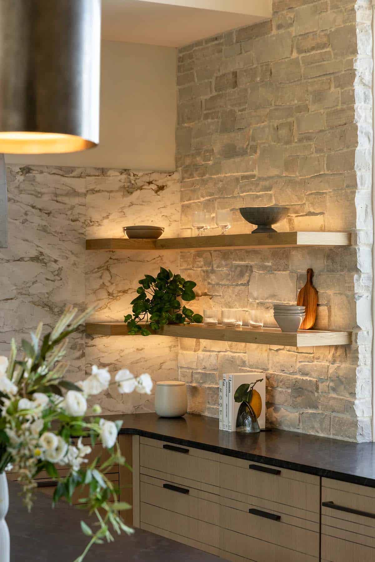 Lit corner shelves against marble backsplash and stone wall in kitchen