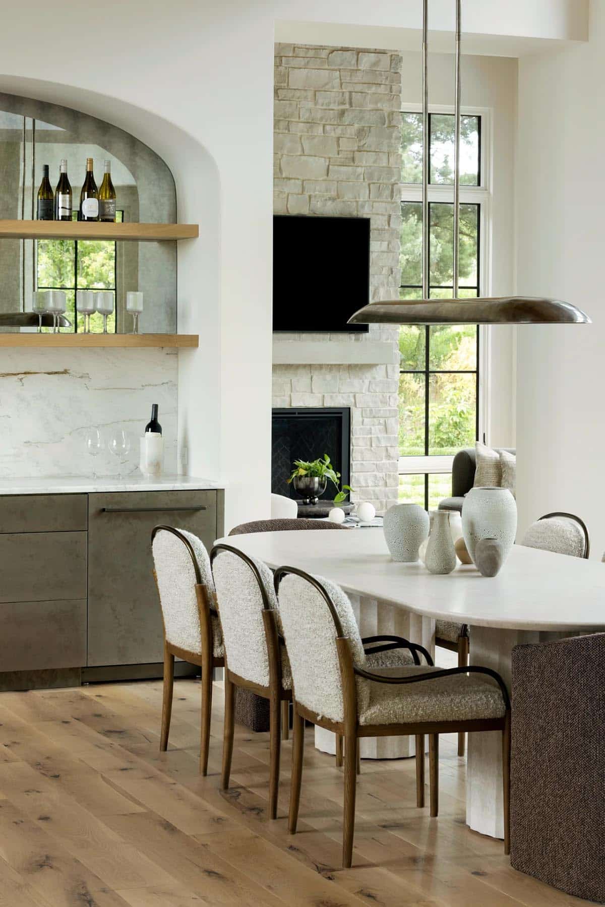 Upholstered dining chairs near arched bar nook and stone fireplace