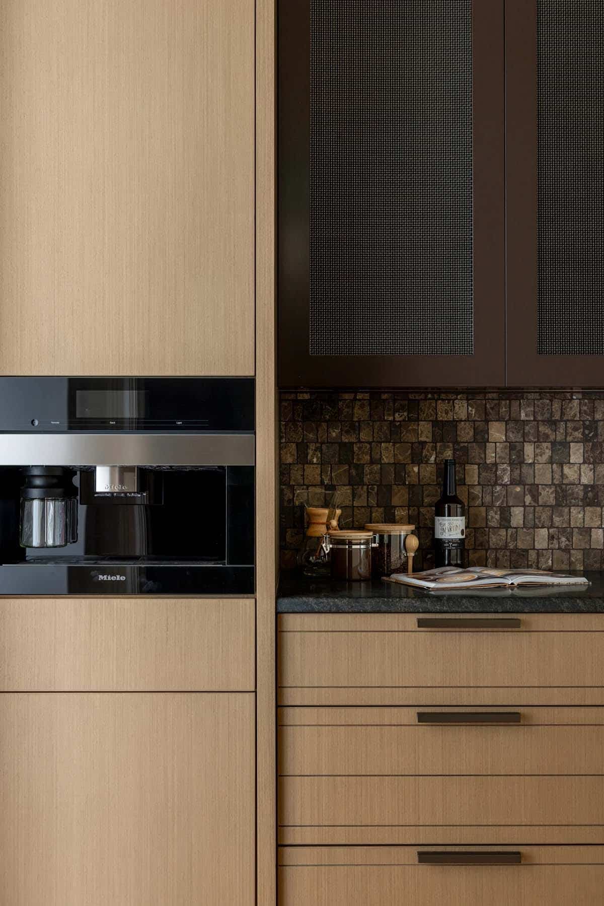 Built-in espresso machine beside mesh-front cabinets and mosaic tile backsplash