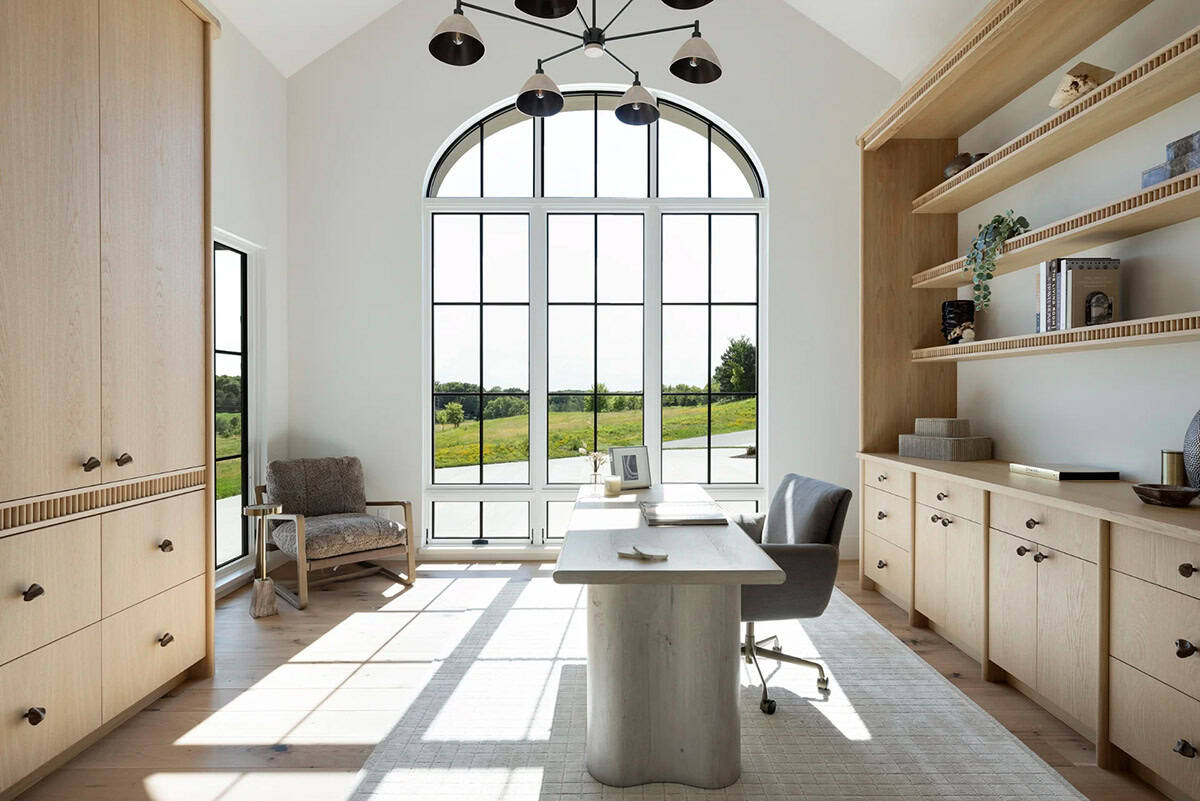Home office with arched window, oak built-ins, and black pendant chandelier