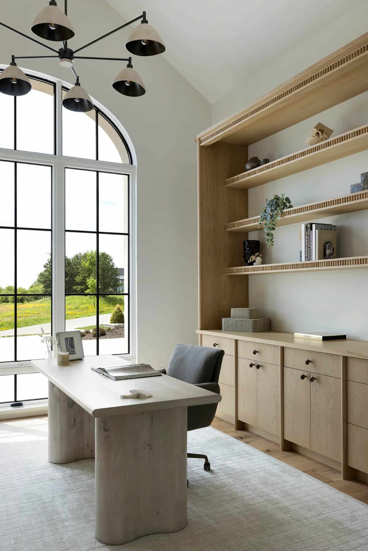 Sculptural desk with curved pedestal base beside fluted oak shelving