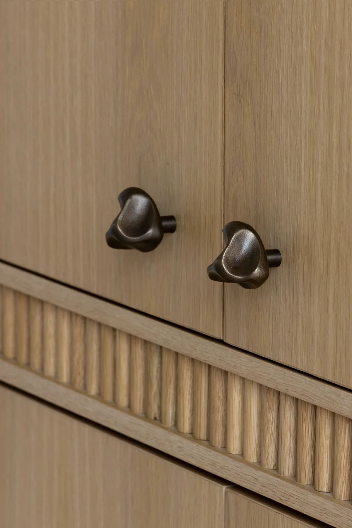 Sculptural bronze cabinet knobs on oak doors above fluted drawer front