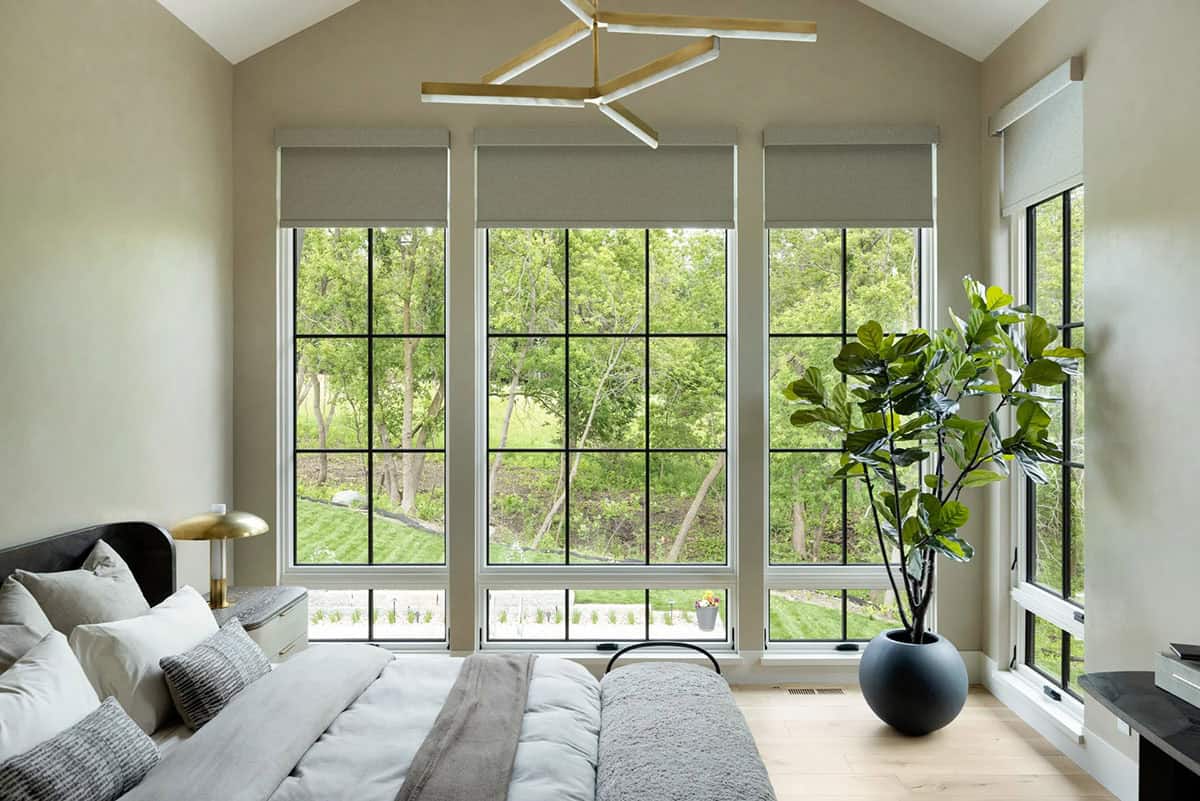Bedroom with tall black-framed windows, roller shades, and brass chandelier