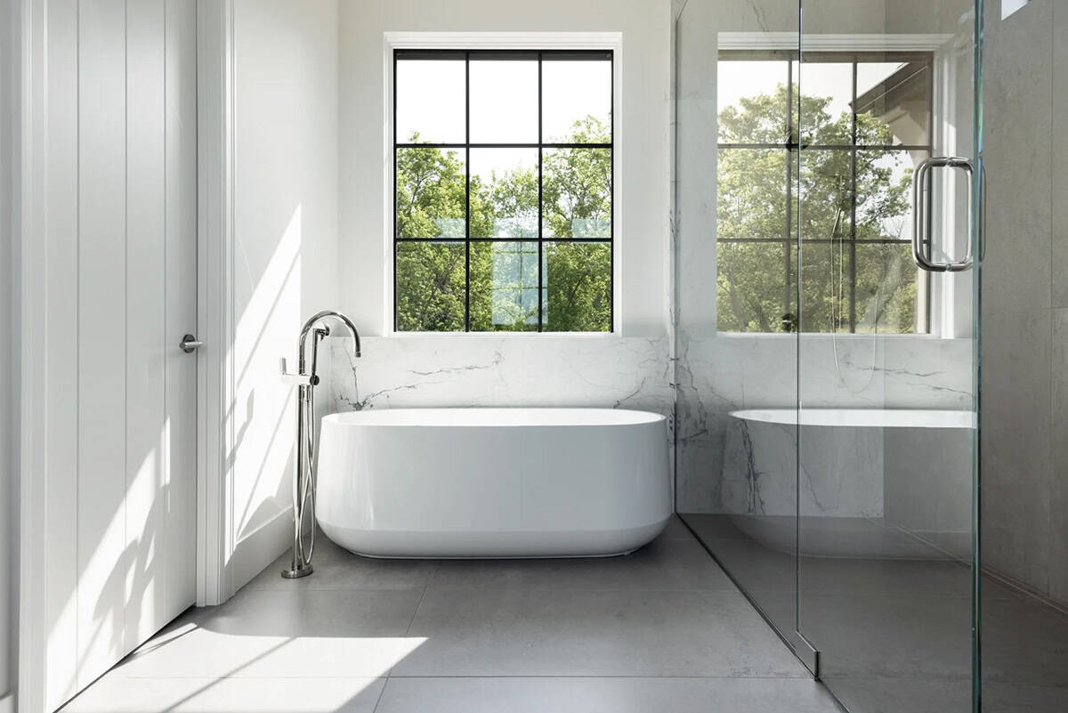 Freestanding white tub beneath black-framed window with marble surround
