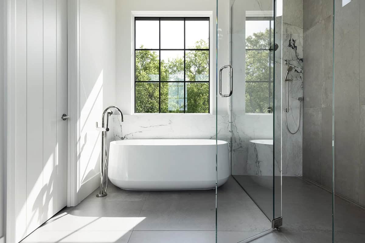 Freestanding tub beside frameless glass shower with marble and gray tile
