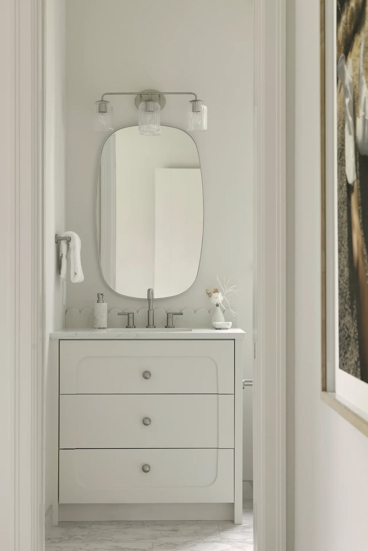 Cream vanity with scalloped backsplash, oval mirror, and ribbed glass light fixture