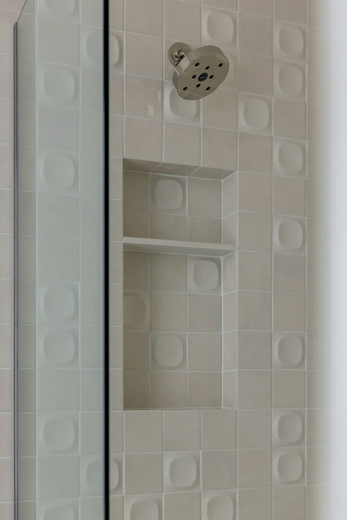 Shower wall with textured square tiles, built-in niche, and polished nickel showerhead
