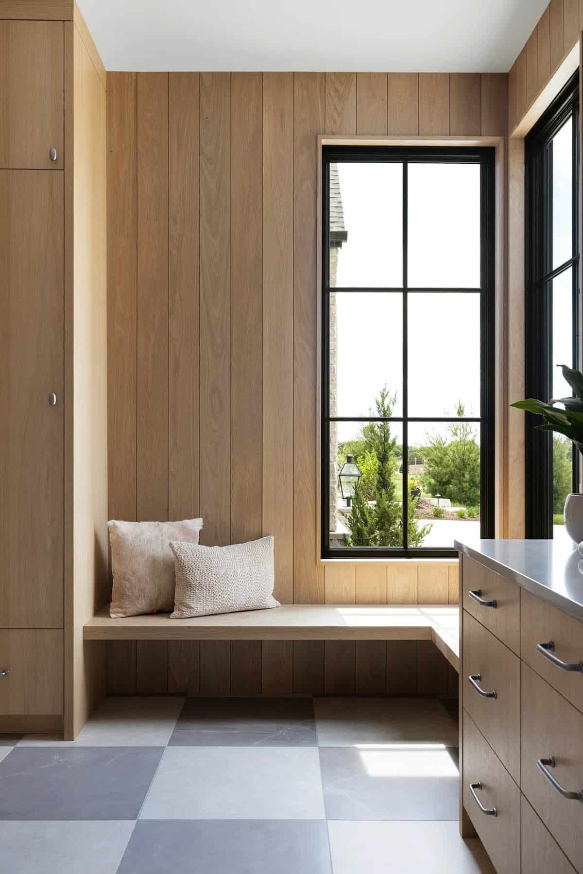 Oak mudroom bench with cushions, tall storage cabinets, and black-framed window
