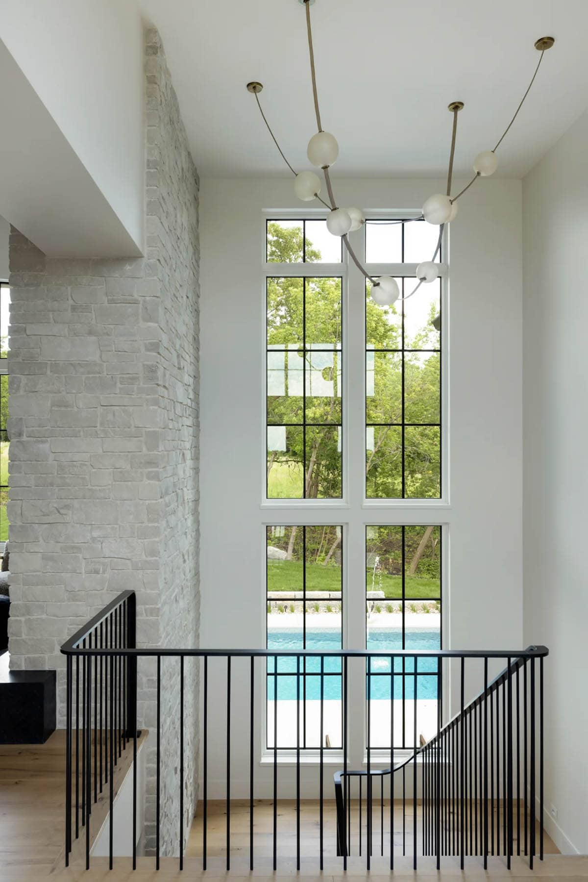 Stairwell with tall windows, black metal railing, and pool view beyond