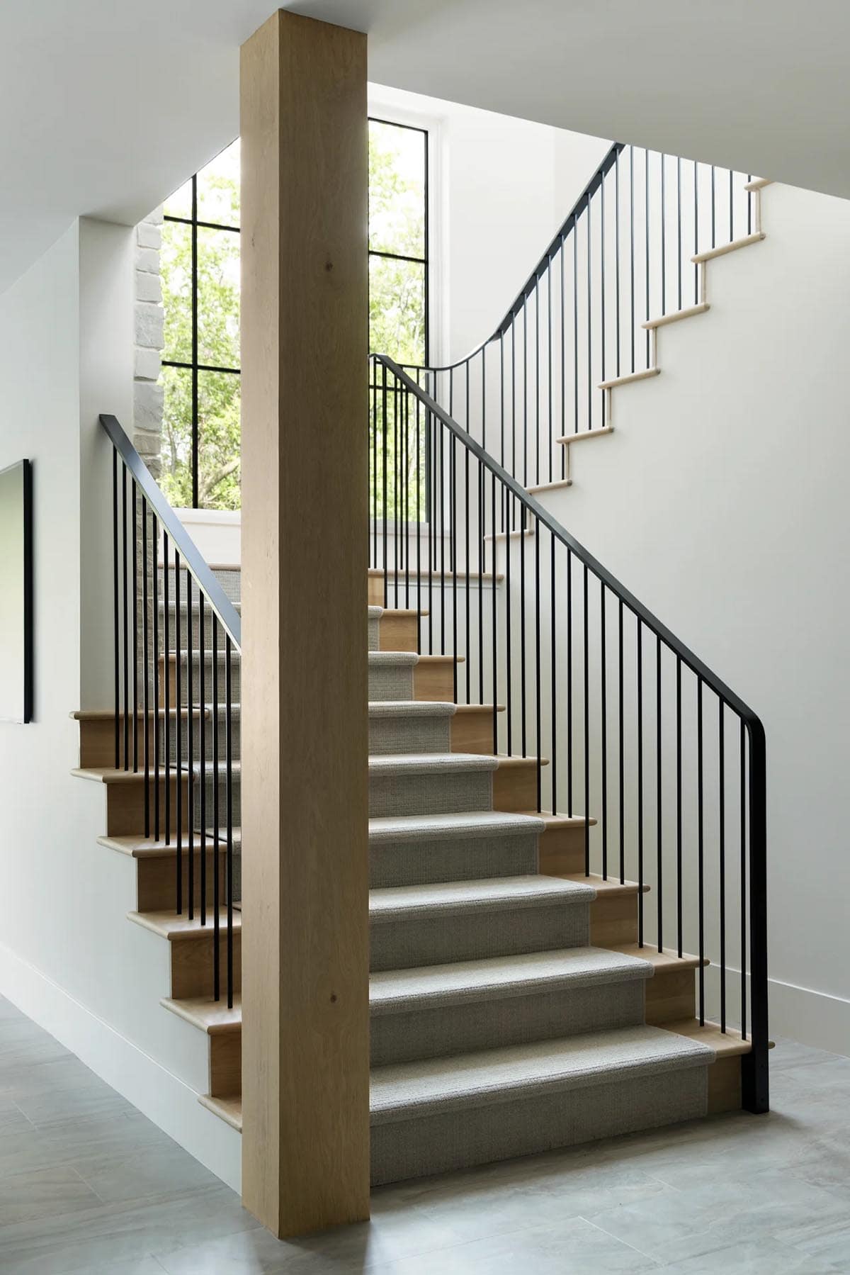 Oak post beside staircase with black metal railing and carpeted treads