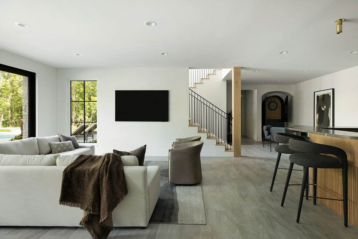 Lower level living area with sectional sofa, bar stools, and staircase beyond