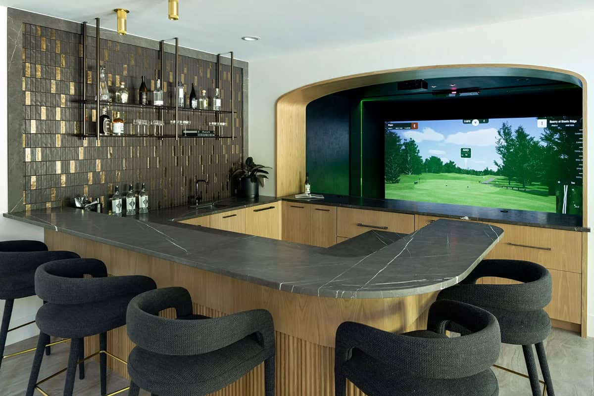 L-shaped bar with stone top, black stools, and golf simulator alcove