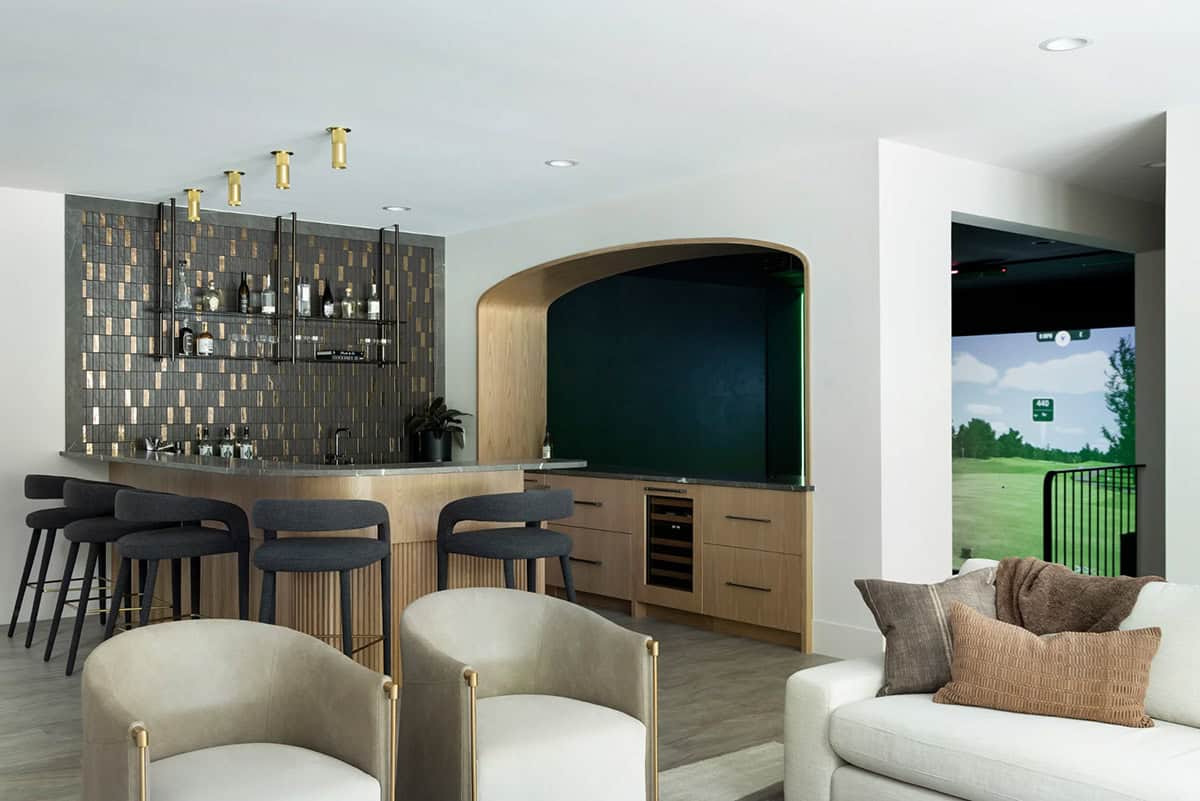 Bar and cream lounge chairs with golf simulator glowing in the background