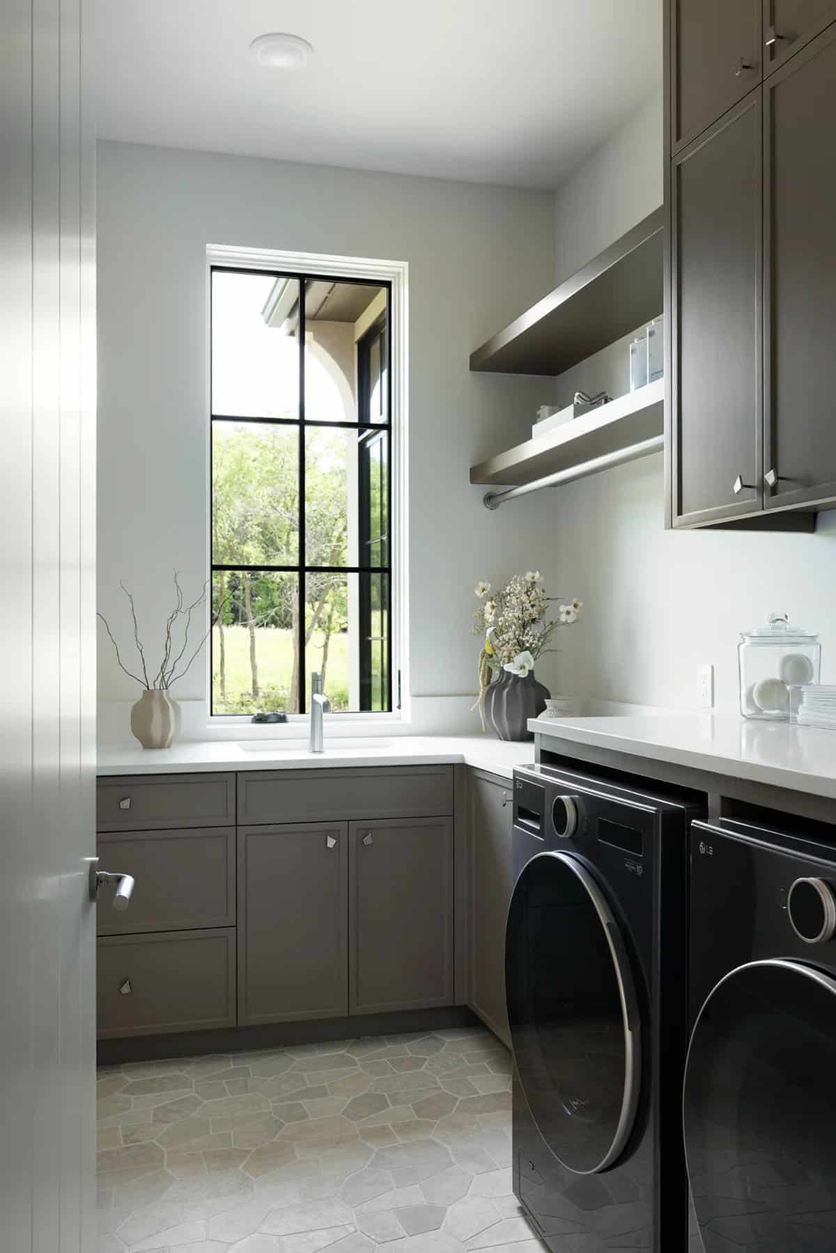 Laundry room with taupe cabinets, floating shelves, and black front-load washer