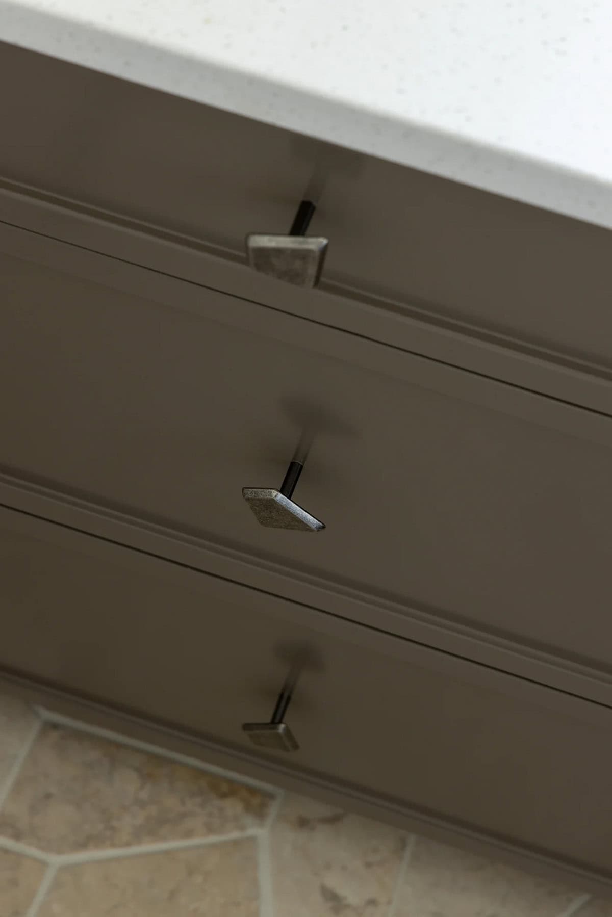 Angular pewter cabinet knobs on taupe drawers above patterned stone floor