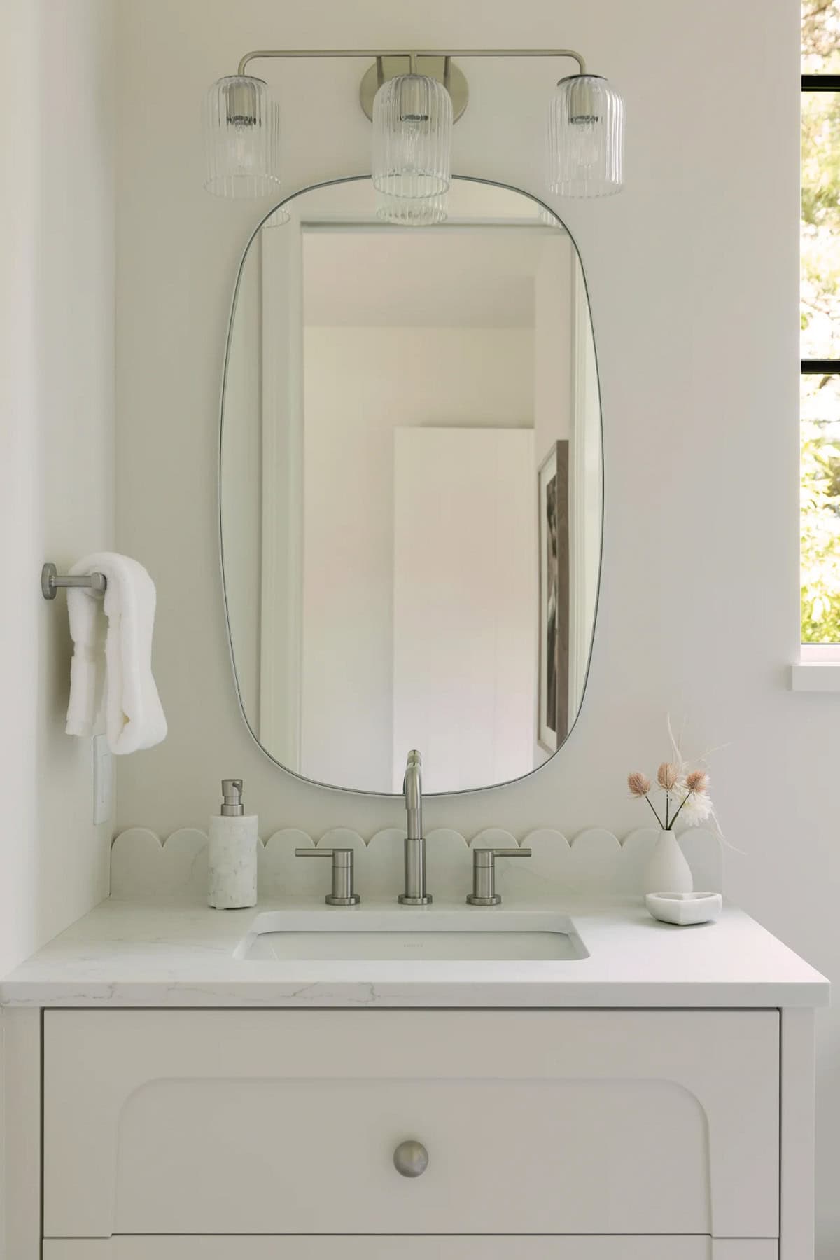 Oval mirror above white vanity with scalloped backsplash and ribbed glass sconce