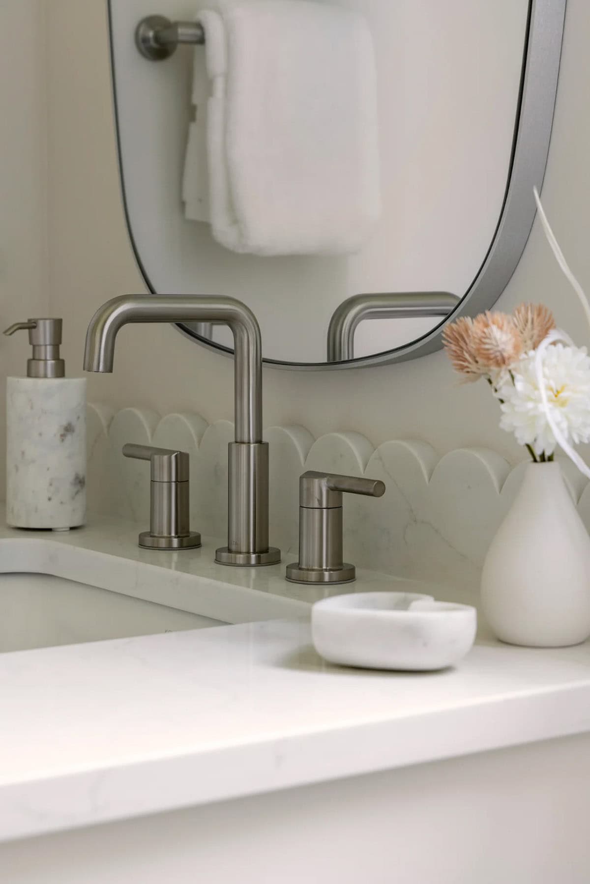 Brushed nickel faucet, scalloped stone backsplash, and marble accessories at sink