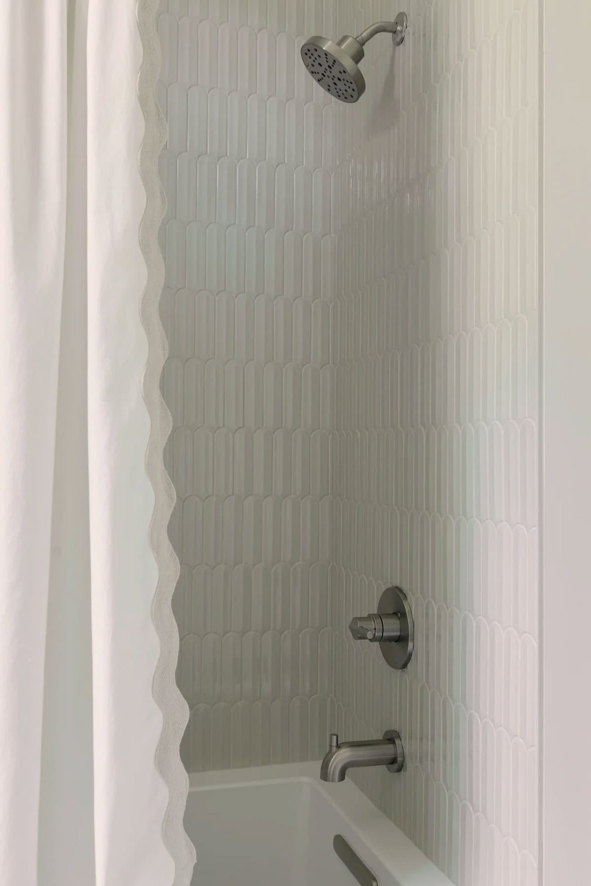Tub shower with arched white tile and wavy-edged shower curtain