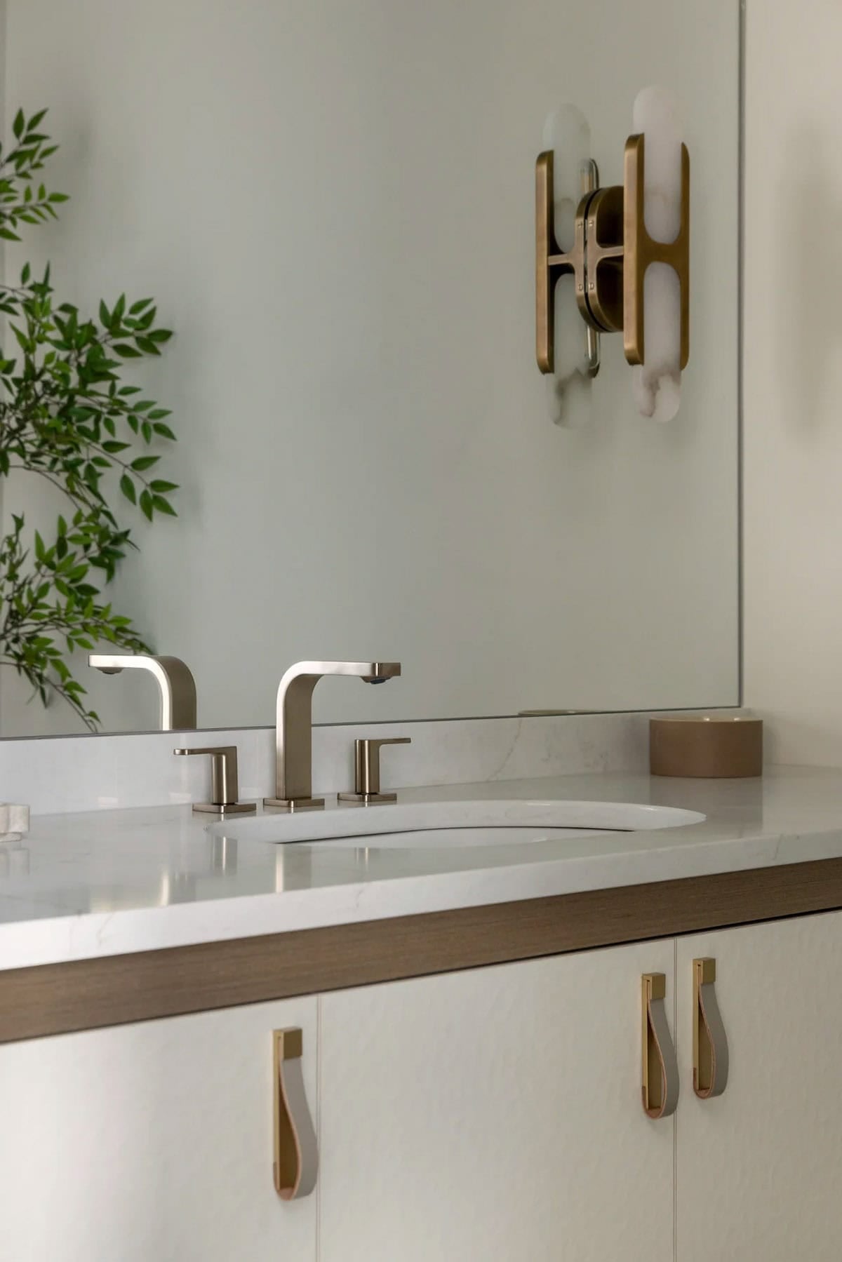 Vanity with leather pull handles, brass alabaster sconce, and brushed nickel faucet