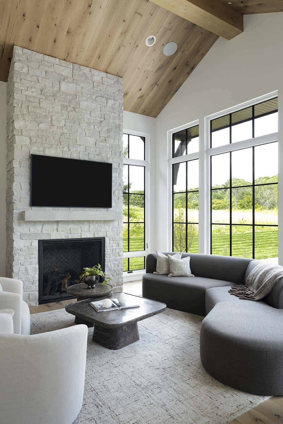 Sunroom with stone fireplace, curved gray sectional, and wood ceiling