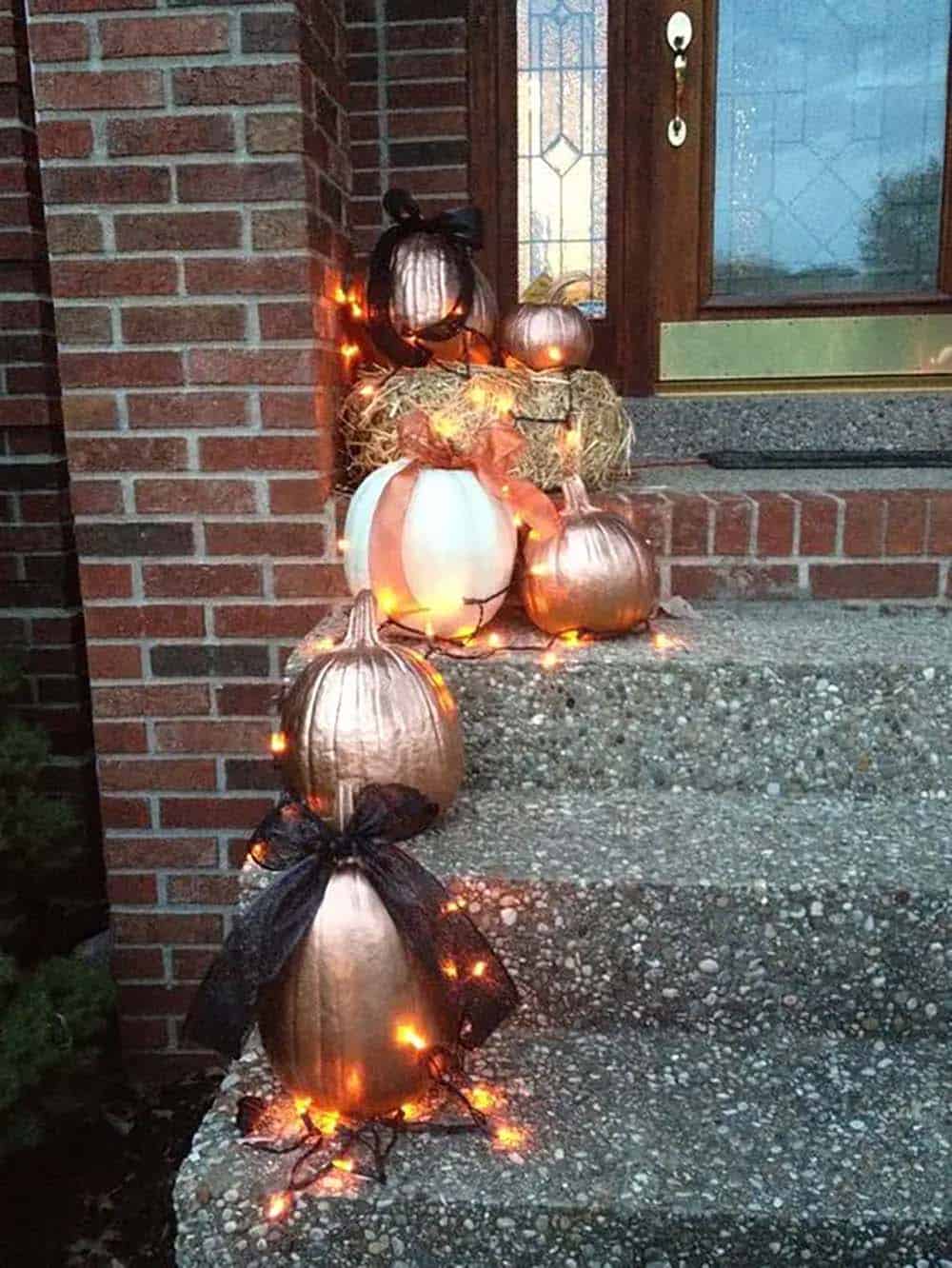 Rose gold pumpkins wrapped in string lights on brick steps