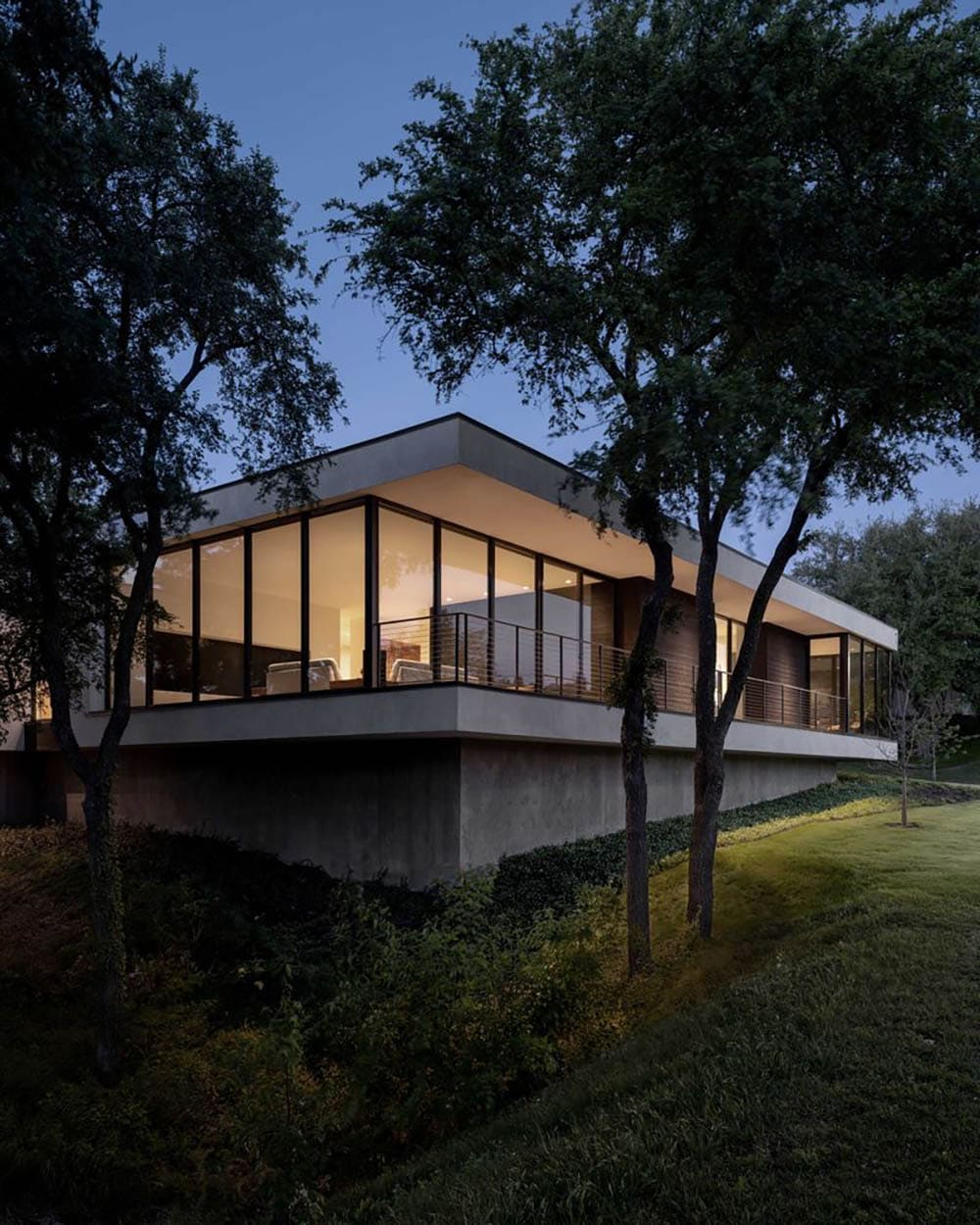 Home nestled among trees on sloped wooded site at dusk