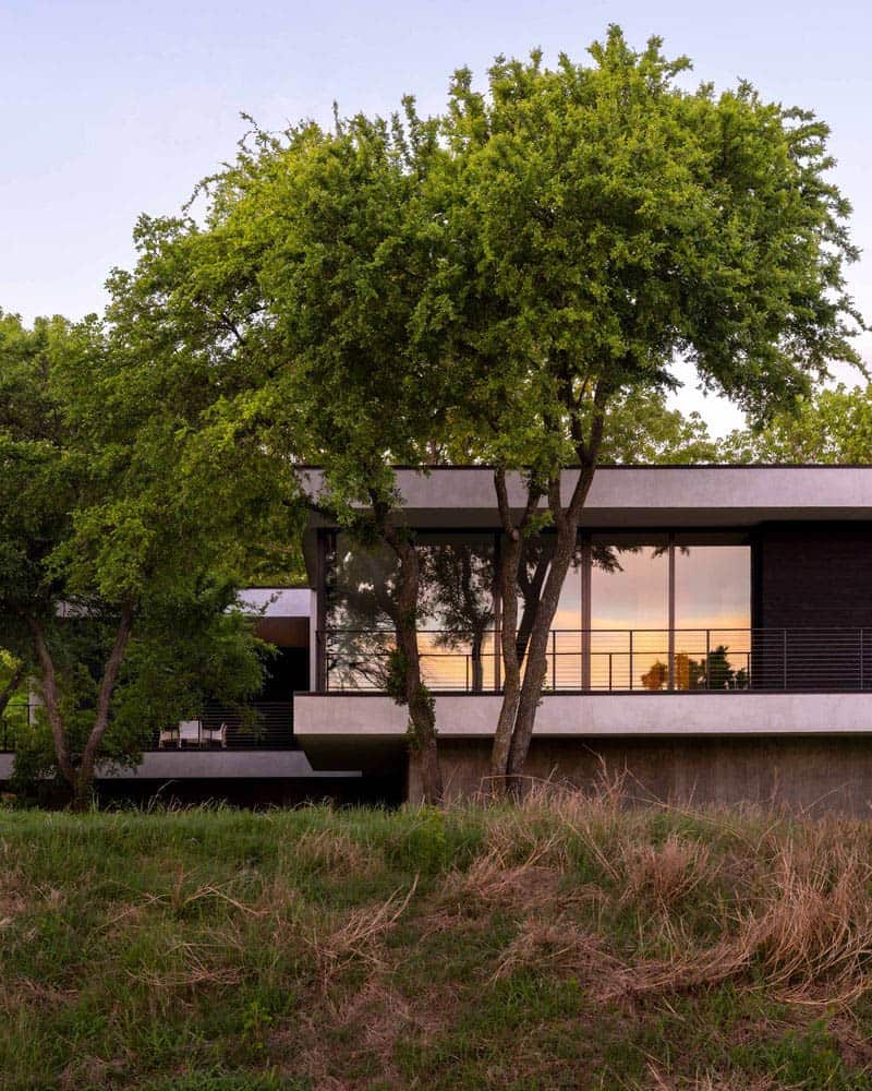 Home exterior through trees at sunset with glowing windows