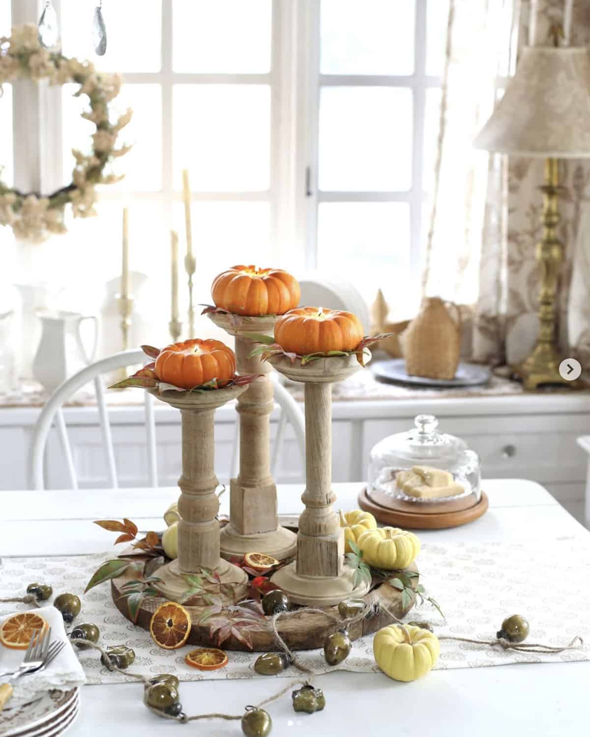 Mini orange pumpkins glowing with tea lights atop tall wooden candlesticks