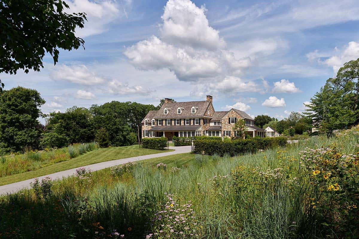 Stone farmhouse sits beyond a native wildflower meadow and curved driveway