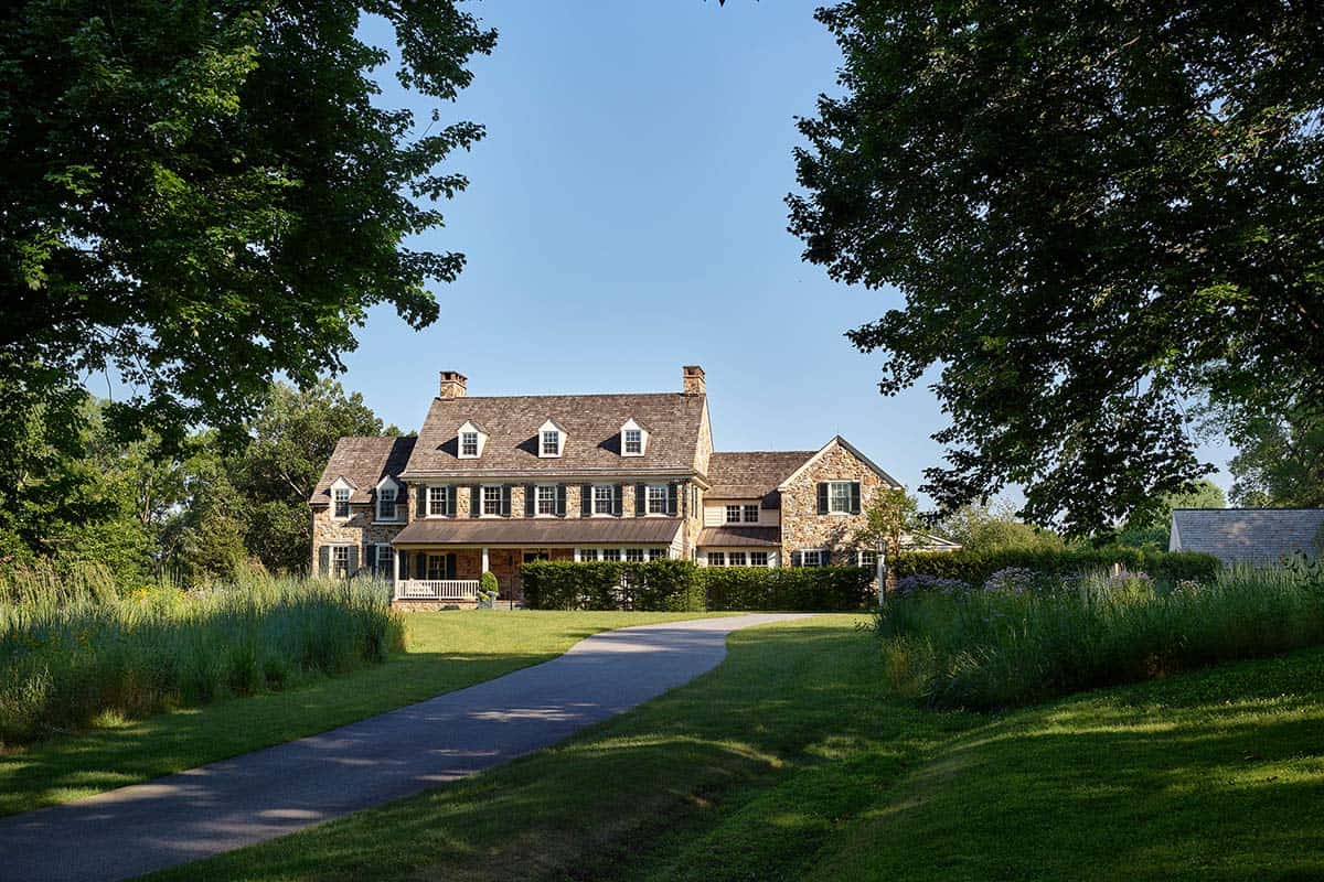 Winding driveway leads through tall grasses toward a stone farmhouse