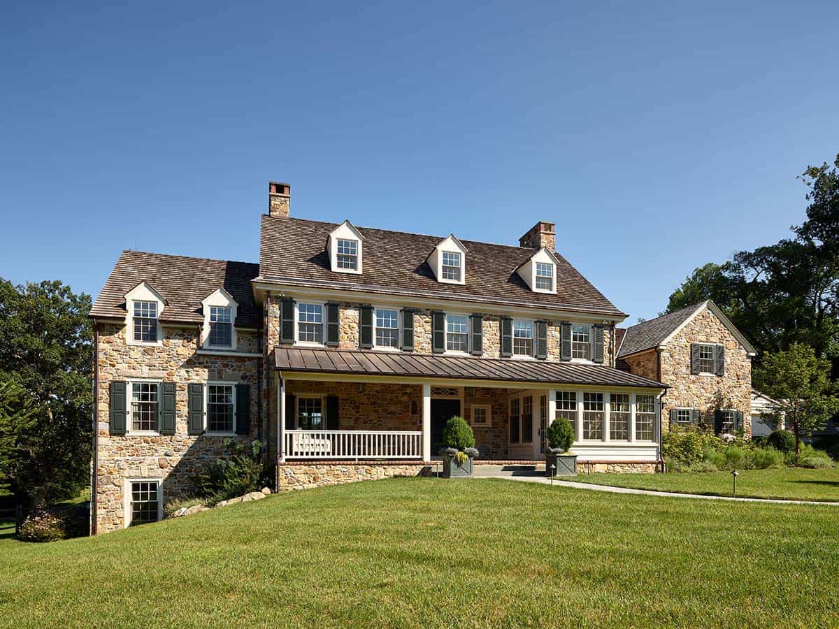 Fieldstone farmhouse facade with green shutters, dormers, and covered porch