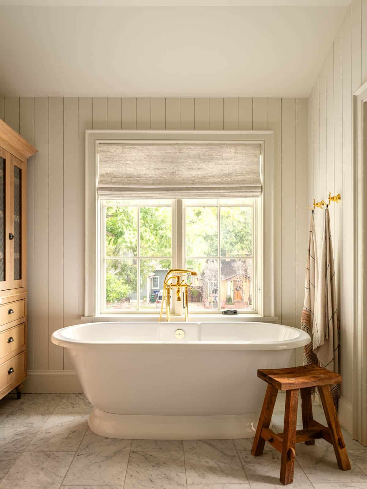 Freestanding tub beneath window with brass floor mounted faucet