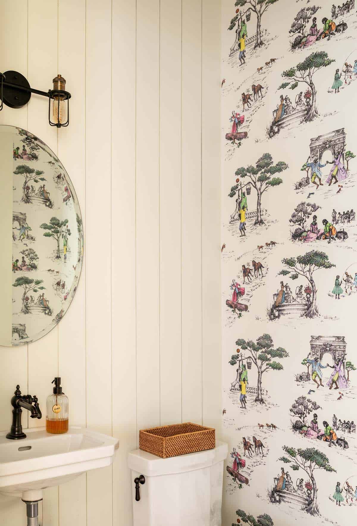 Powder room with scenic toile wallpaper and round vintage mirror