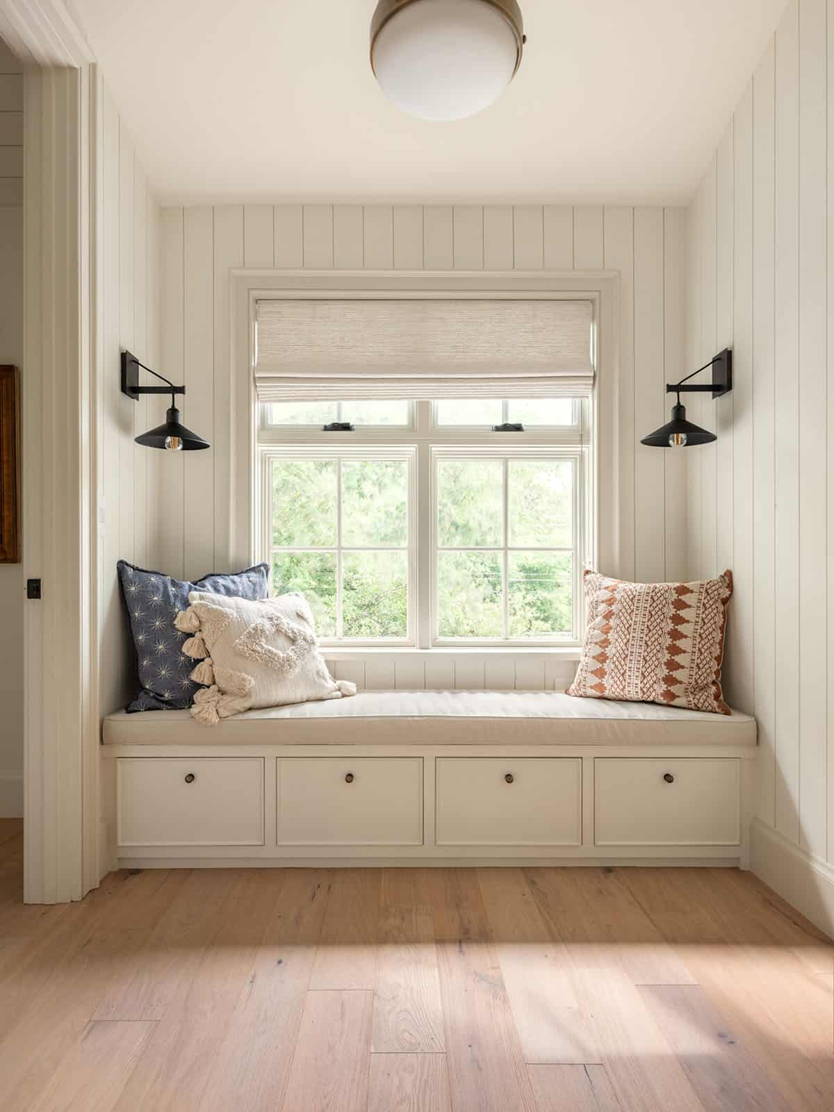 Window seat nook with black sconces and patterned throw pillows