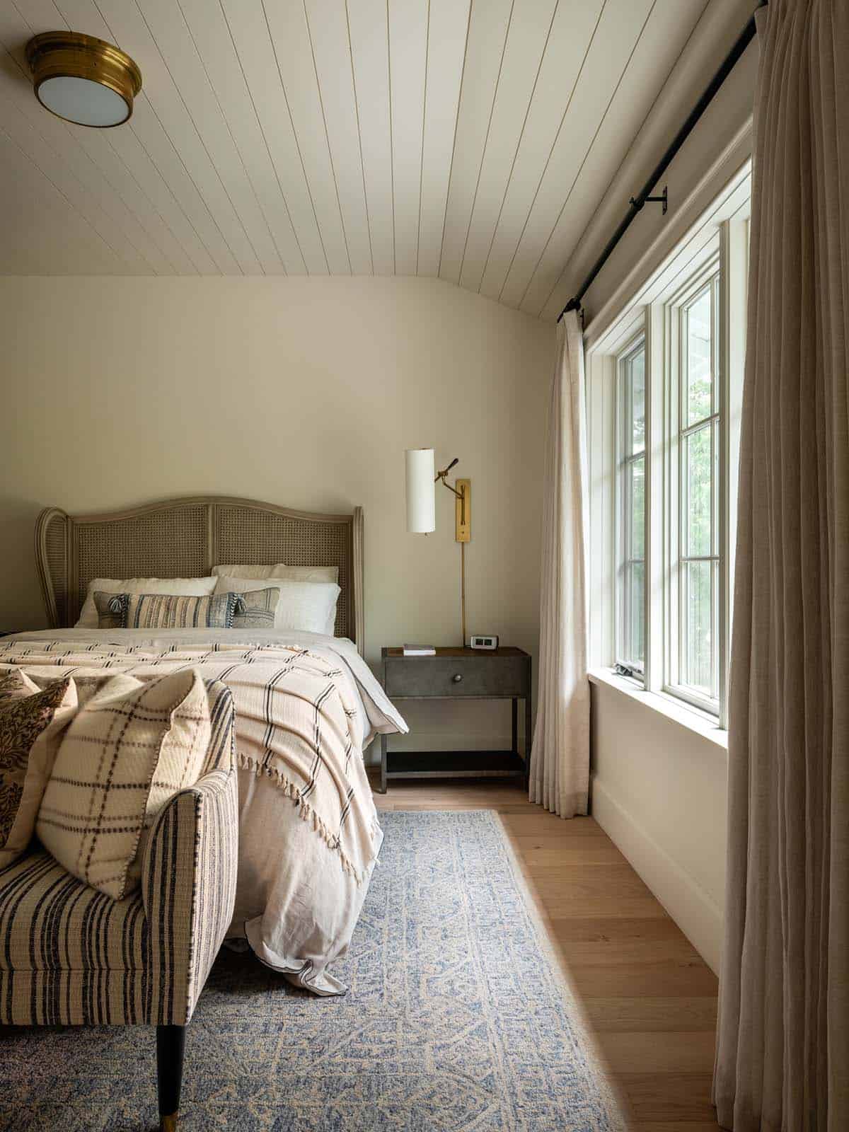Bedroom with cane headboard, blue rug, and draped curtains