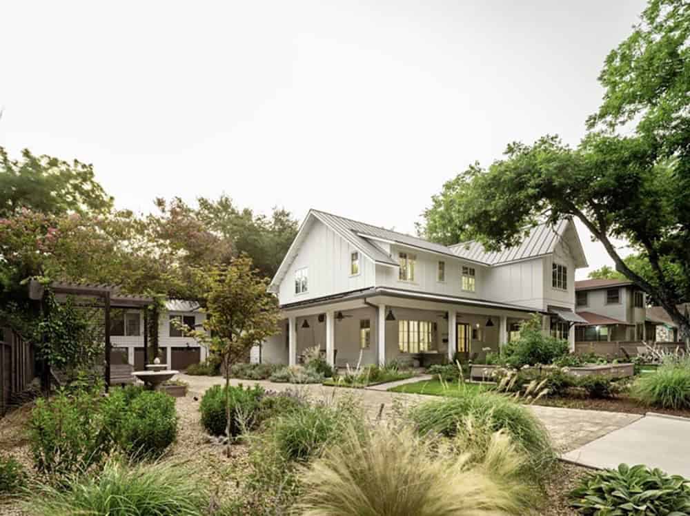 White farmhouse exterior with metal roof and mature shade trees