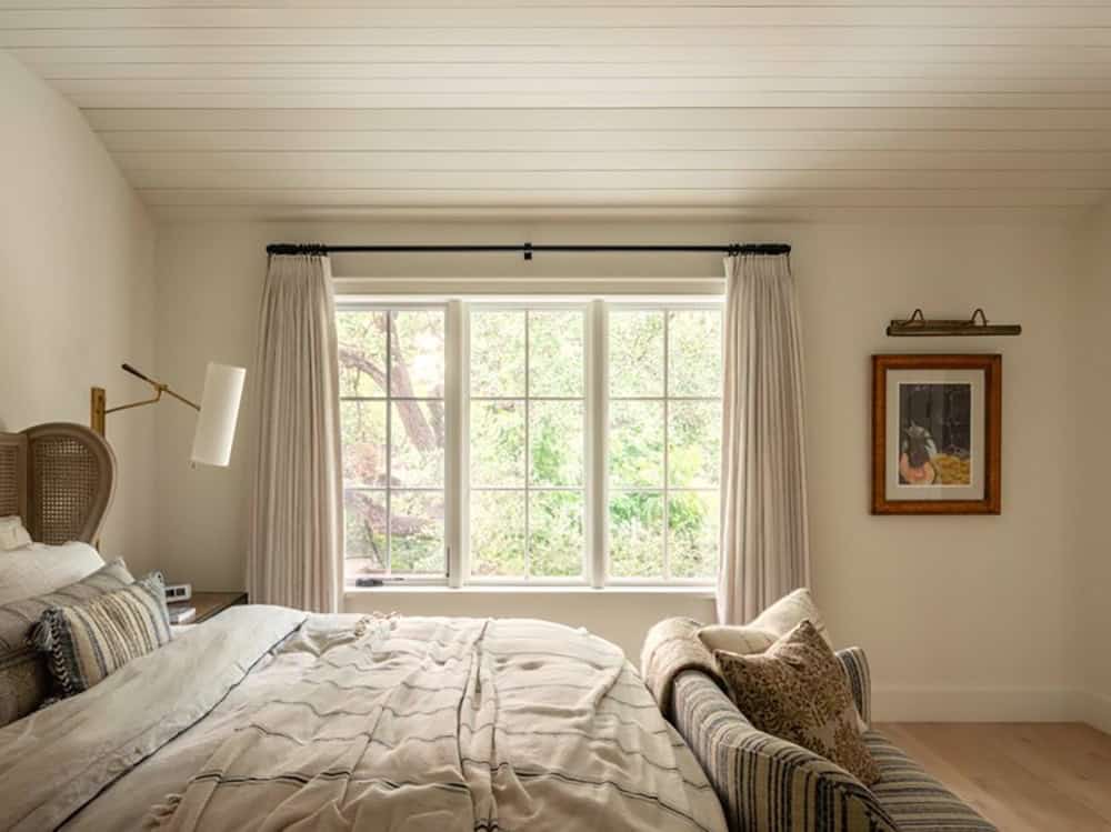 Bedroom with cane headboard, striped bench, and wooded window view