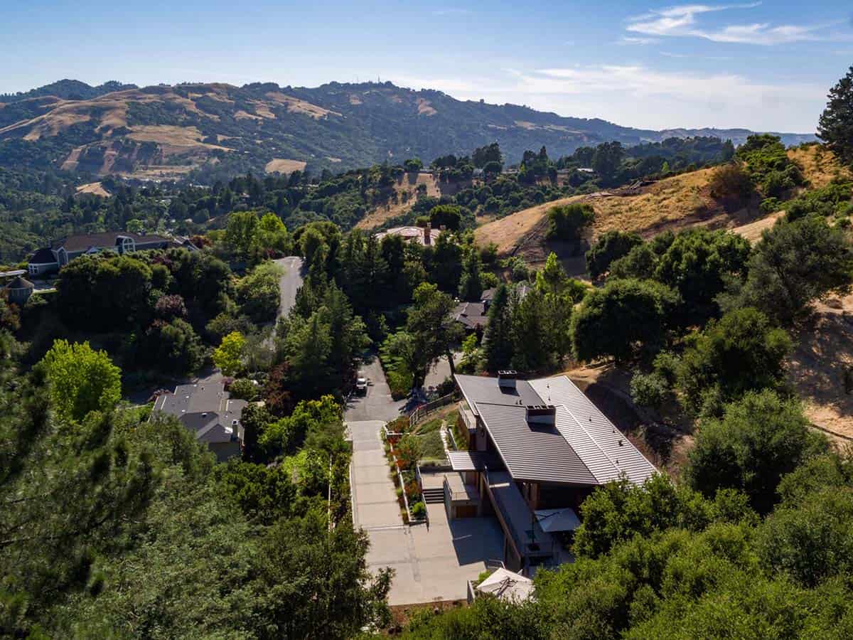 Aerial view of modern hillside home overlooking wooded canyon and distant hills