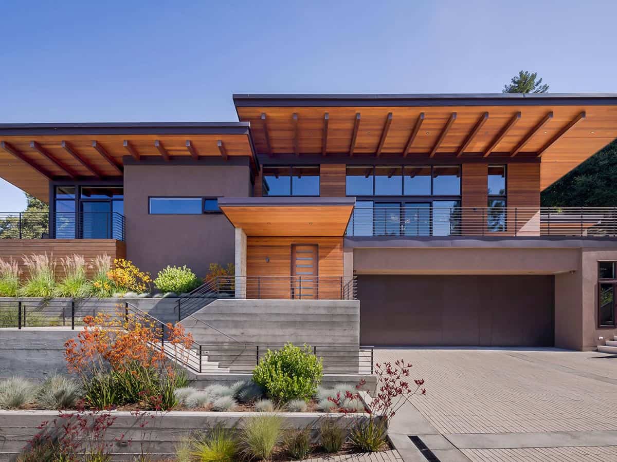 Front entry framed by wood soffit, concrete steps, and layered retaining walls