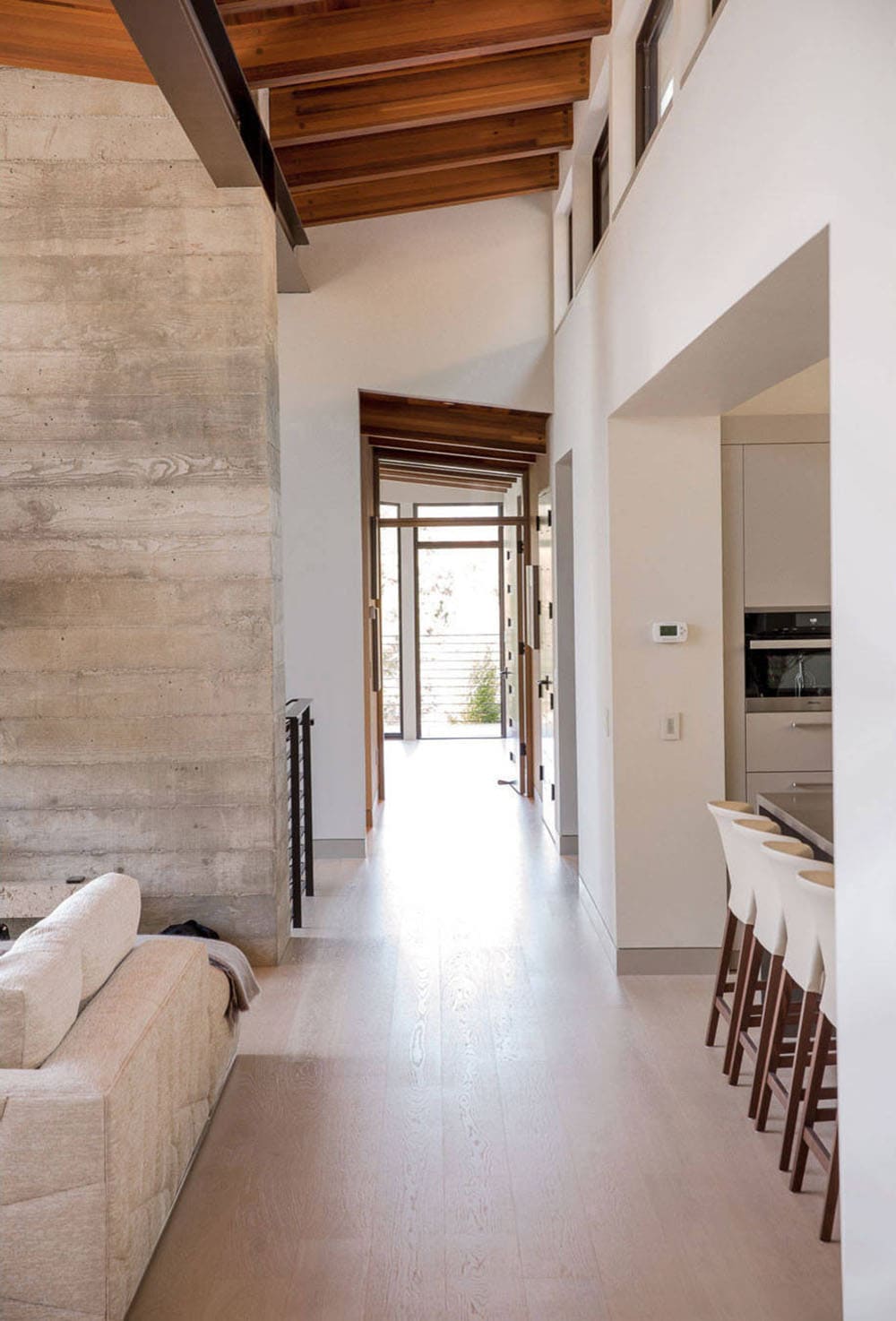 Open hallway leads past kitchen island toward glass entry doors and deck