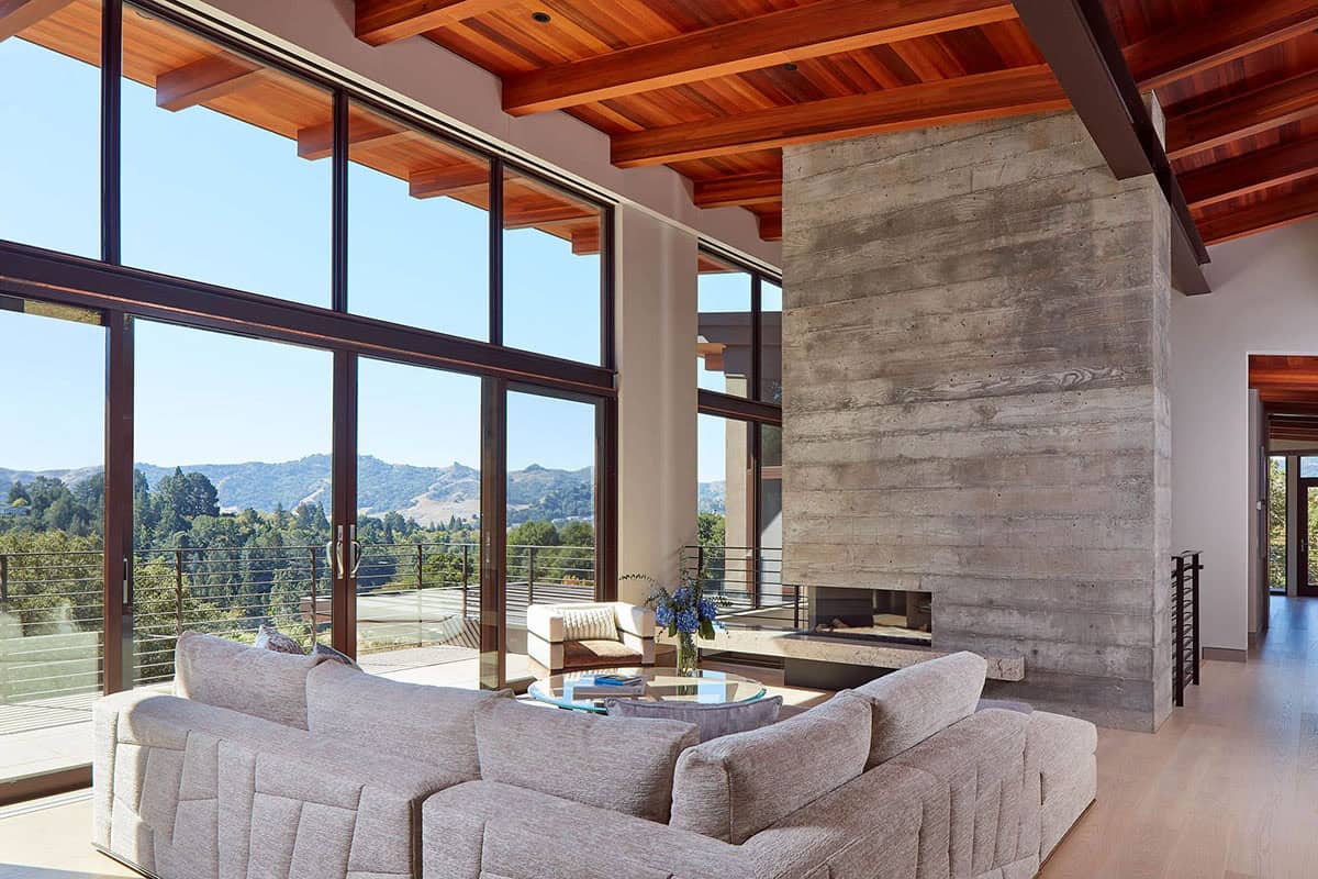 Living room sectional faces concrete fireplace with panoramic hillside window views