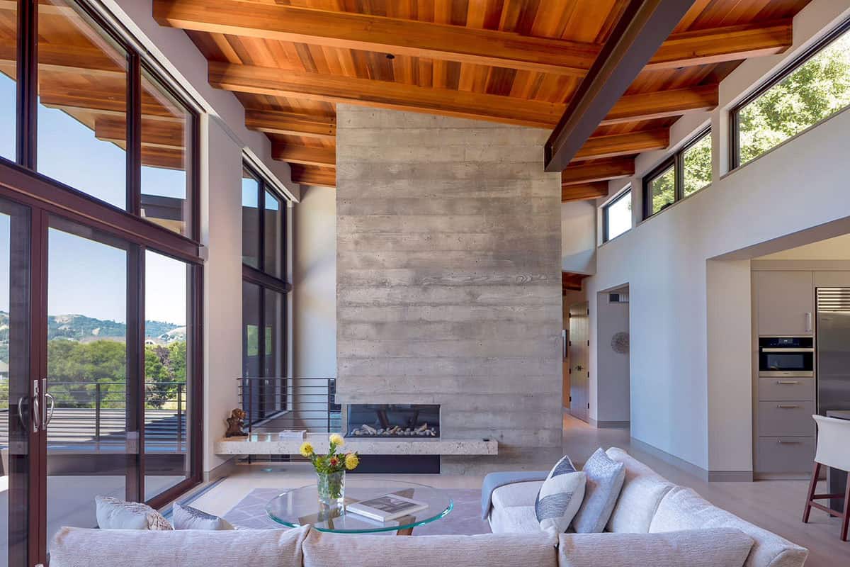 Living room with double-height windows, concrete fireplace, and cedar beam ceiling
