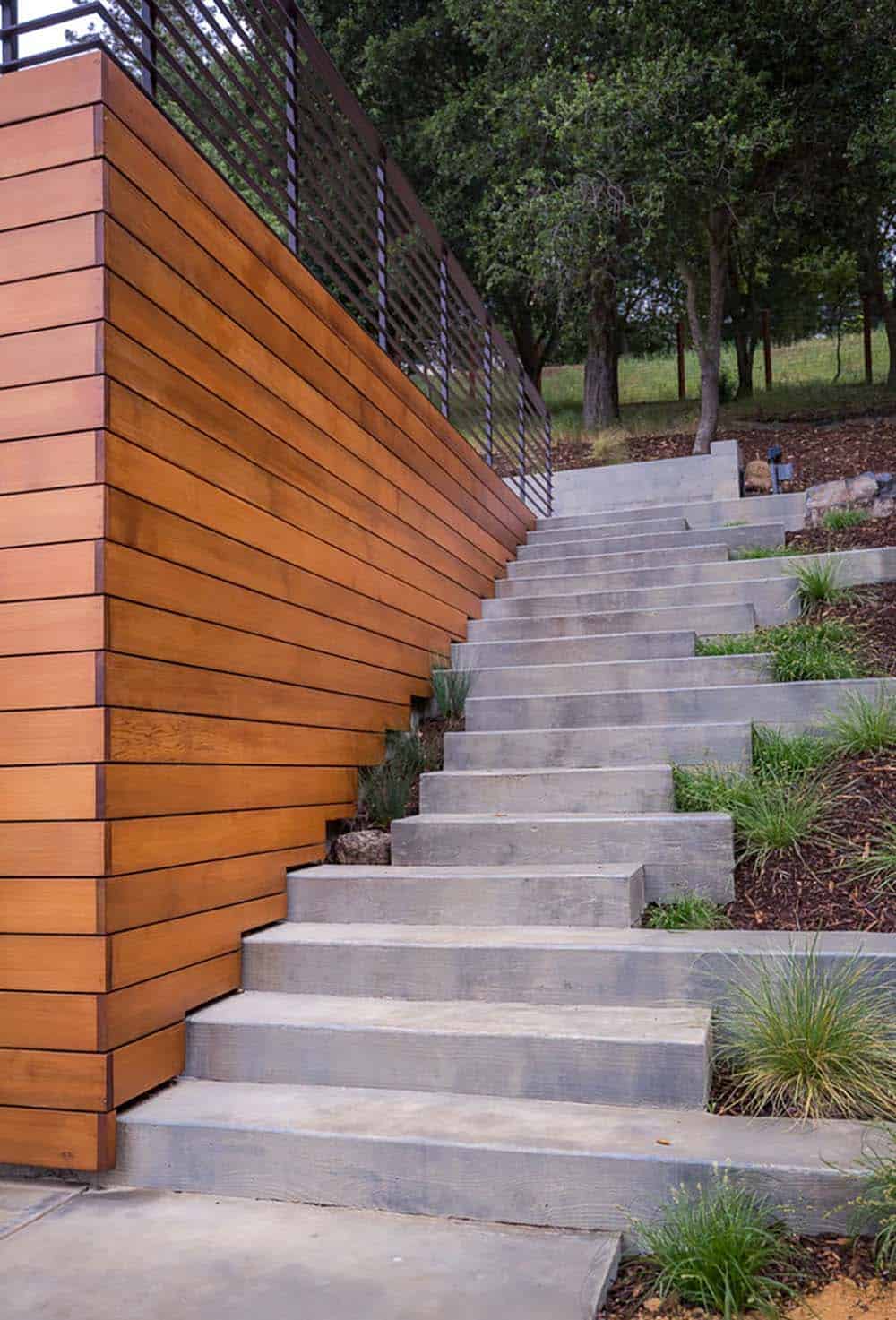 Cedar-clad wall borders concrete stairway leading up wooded hillside slope