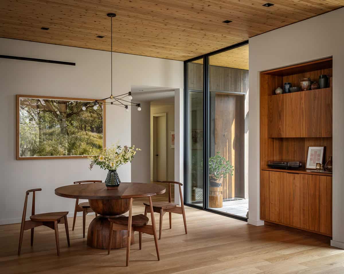 Round walnut dining table with sculptural base beside a built-in walnut cabinet