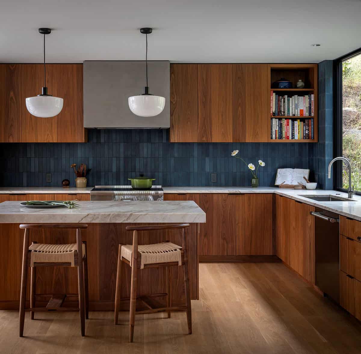 Walnut kitchen with blue tile backsplash, stone island, and woven counter stools