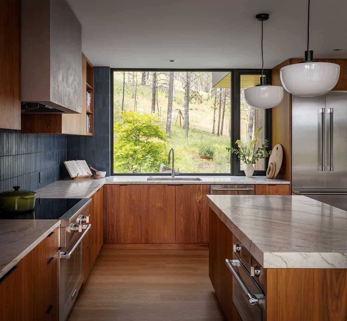 Kitchen sink beneath a large window framing forest and hillside views